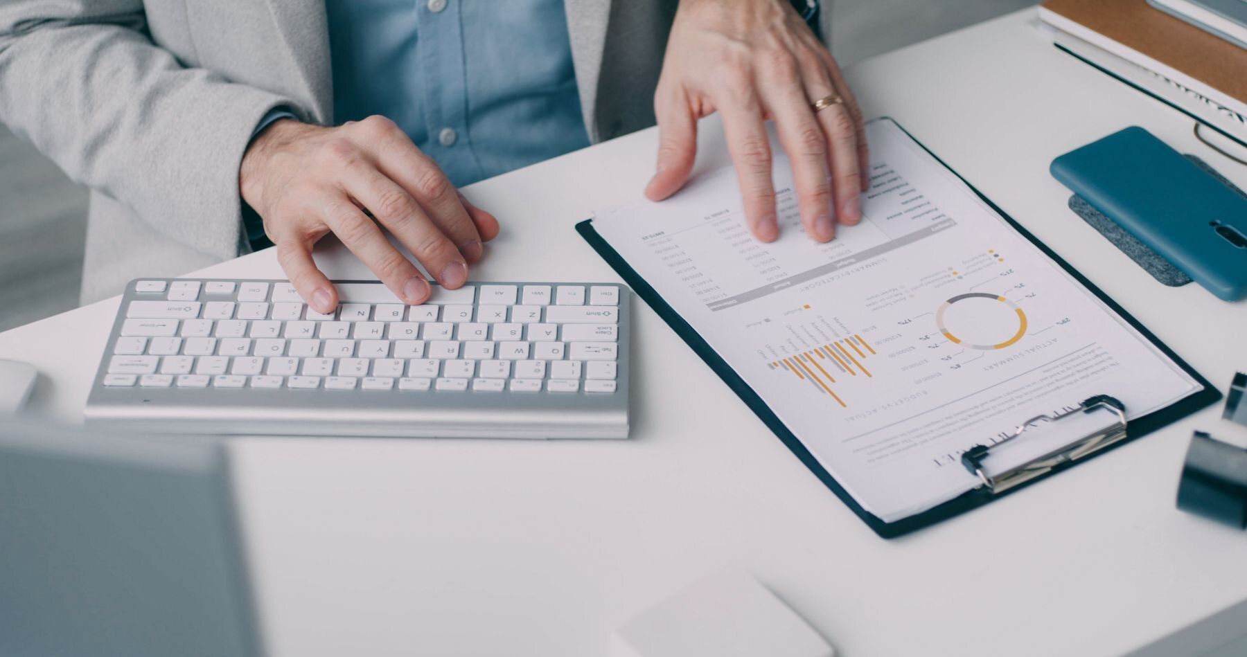 Profissional analisando relatório financeiro com gráficos em uma prancheta ao lado do teclado