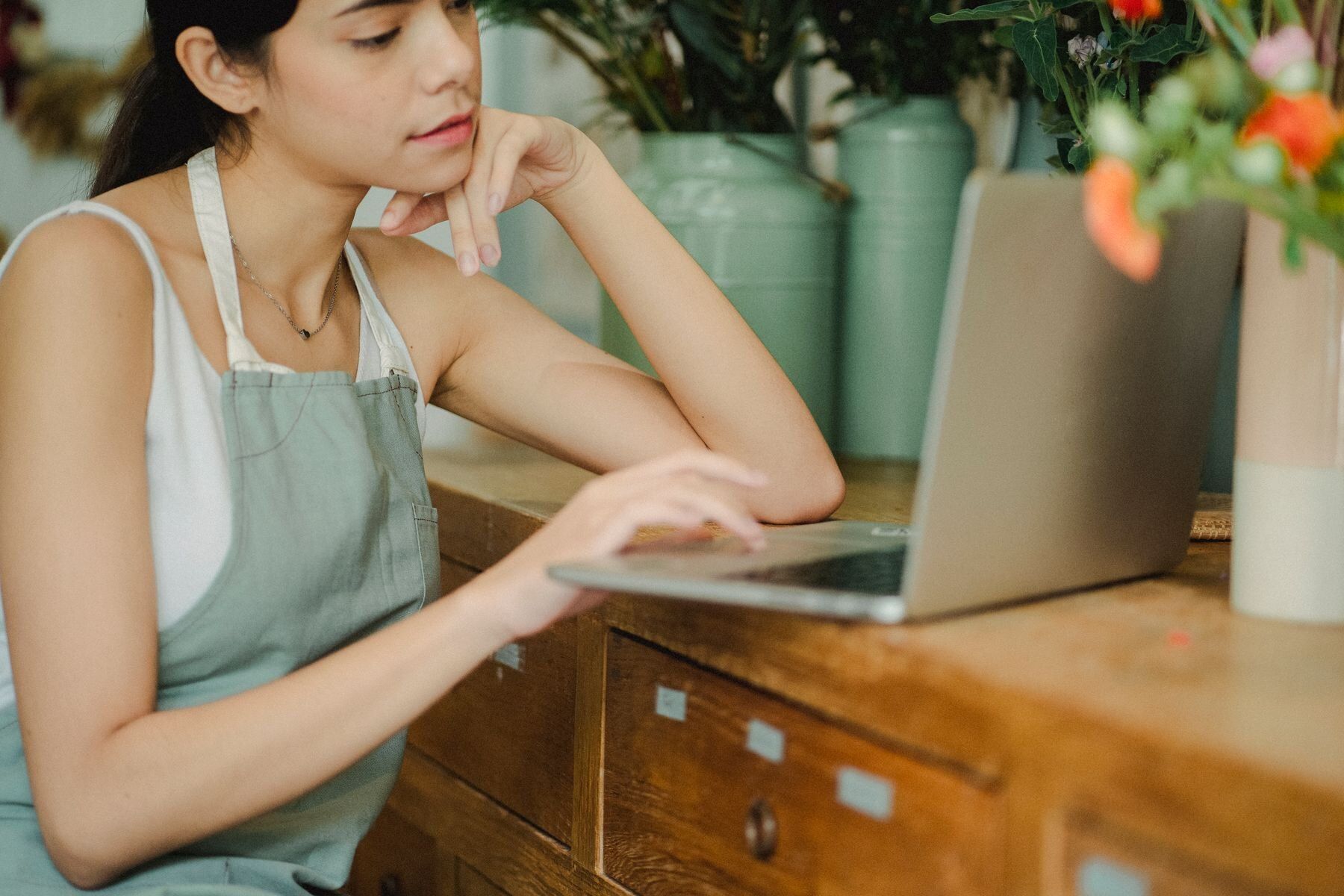 Empreendedora de avental usando o notebook no balcão de madeira da sua floricultura